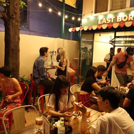 The terrace at East Borough at night — string lights, red stools, and a full crowd eating outside.